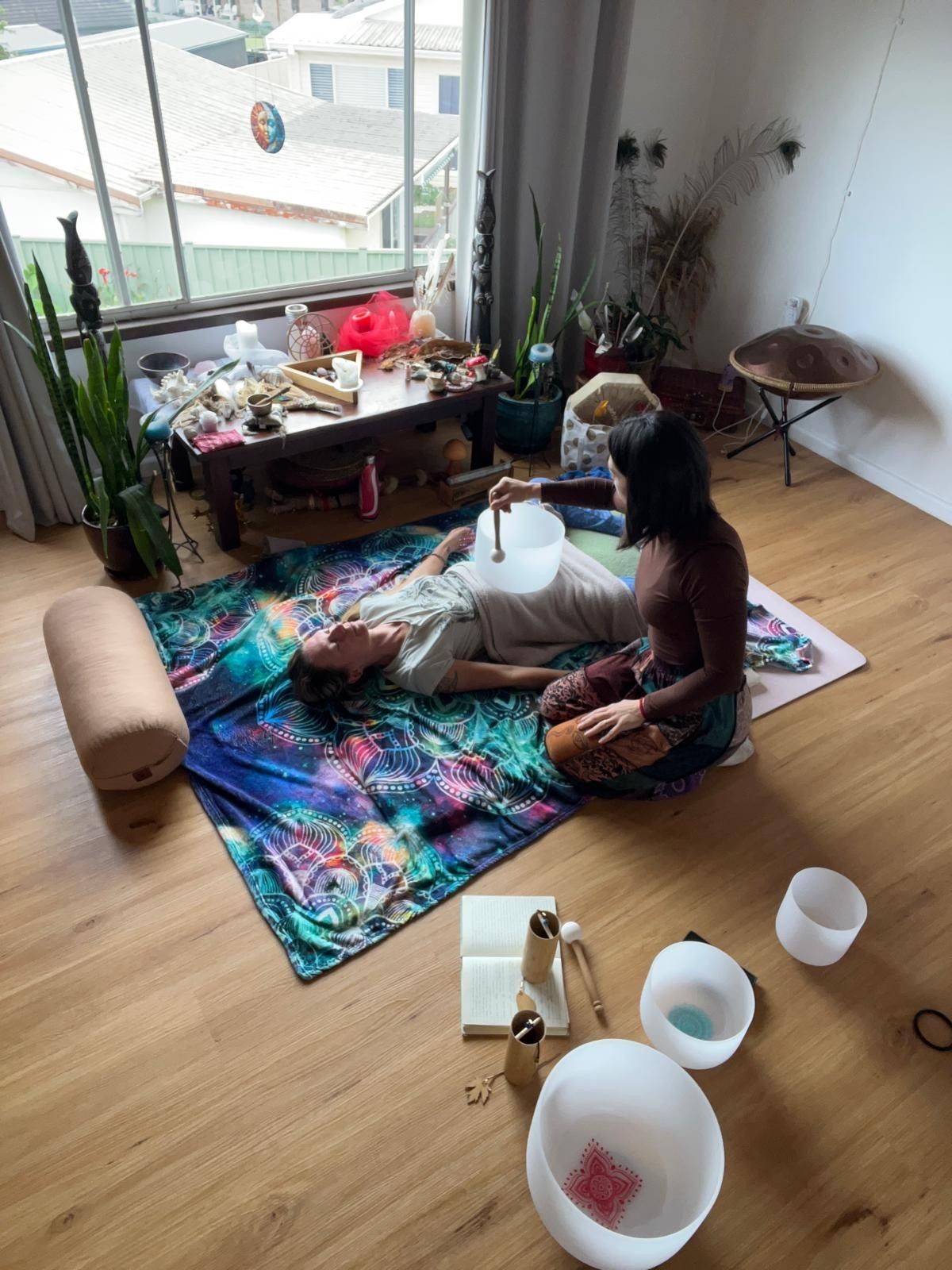 Person playing a singing bowl during a meditation session indoors with colorful rug and floor cushions.